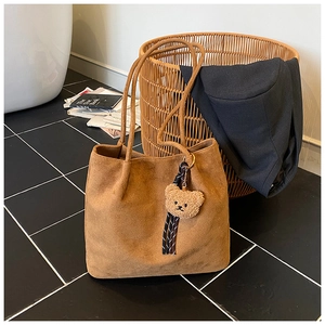 Close-up of brown suede tote bag featuring a cute teddy bear charm and striped ribbon detail