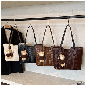 Detail of four woven leather tote bags in various colors hanging on a minimalist metal rack