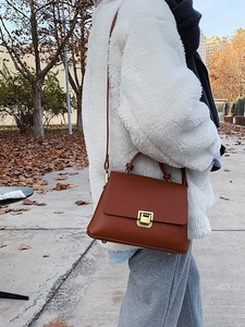 Vintage brown leather crossbody bag with gold buckle in an autumn park setting