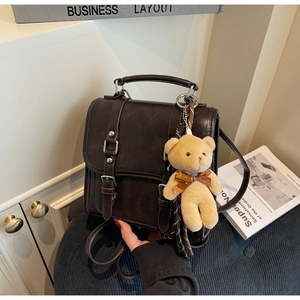 Detail view of dark brown vintage faux leather messenger bag with plush bear charm