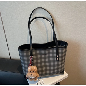 Detail of grey checkerboard tote bag with brown plush puppy charm on design book