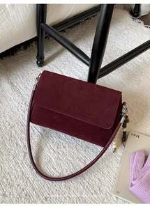 Detail of burgundy suede crossbody bag with wooden bead charm on a soft textured carpet