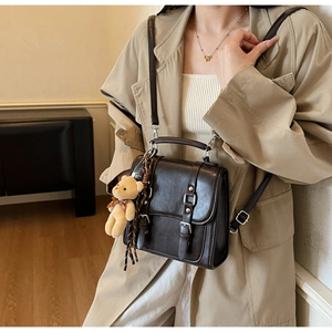 Detail view of dark brown vintage crossbody bag with bear charm and metallic buckle straps