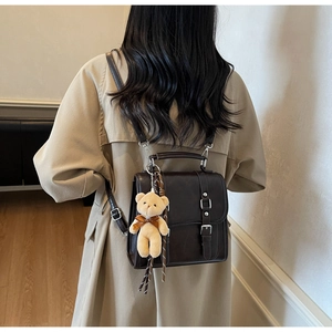 Detail of vintage dark brown faux leather backpack with metallic buckles and plush bear charm