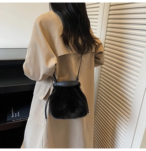 Detailed close-up of a black plush faux fur bucket bag with drawstring and leather strap