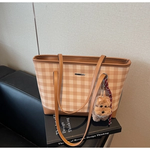 Detail of checkered tote bag with brown handles and a cute plush dog charm on a book