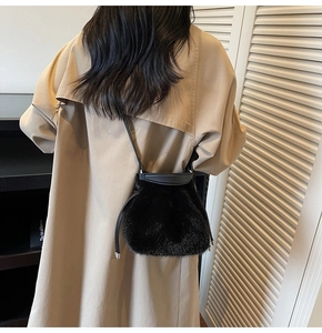 Detail of plush black faux fur bucket bag worn over a beige coat for winter style