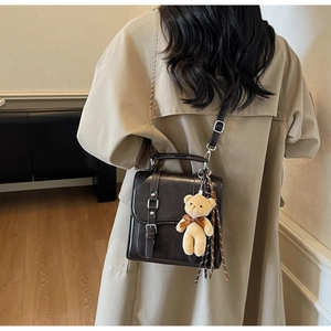 Detail view of retro crossbody bag with vintage buckle straps and plush bear charm accent