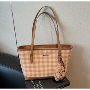 Close-up of brown plaid tote bag featuring premium leather handles and a plush dog charm