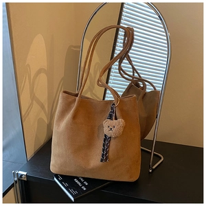 Detailed macro view of brown suede tote bag with cute bear charm and striped ribbon