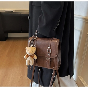 Detail of vintage brown leather satchel with bear charm and adjustable shoulder strap