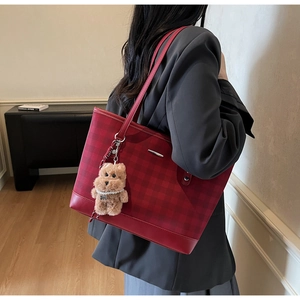 Detail of red plaid tote bag featuring a leather handle and a cute plush bear charm