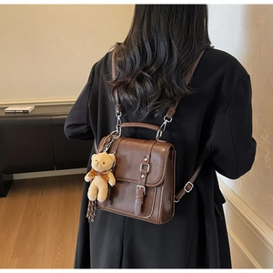 Detail of vintage brown leather mini backpack with decorative buckle straps and plush bear charm