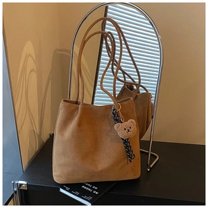 Detail of a brown suede tote bag with a cute plush bear charm on a dark surface