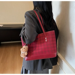 Detail shot of a red plaid tote bag with a plush bear charm on a model's shoulder