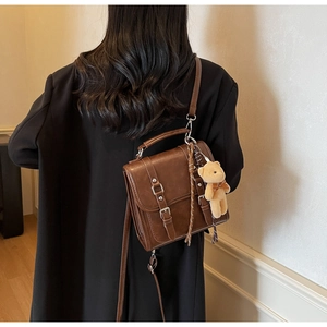 Detail of vintage brown leather satchel with plush bear charm and classic double buckle