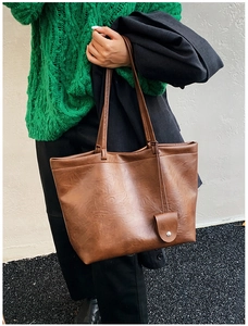 Close-up of a brown textured faux leather tote bag on a model wearing green knitwear