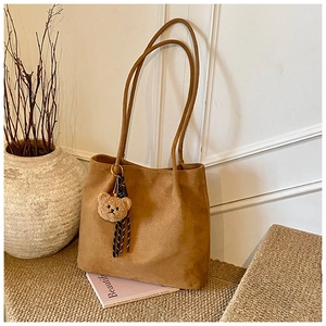 Close-up of brown suede tote bag with cute plush bear charm and striped ribbon details