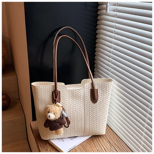 Detail of cream woven tote bag with brown leather straps and a plush bear pendant charm