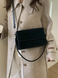 Minimalist black matte leather crossbody bag with dual straps shown on a beige coat