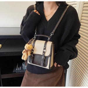 Detail of two-tone vintage faux leather backpack with decorative buckles and plush bear charm