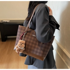 Detailed close-up of brown plaid tote bag with cute plush bear pendant and pearl chain