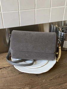 Minimalist grey suede crossbody bag with wooden bead charm on a white ceramic plate