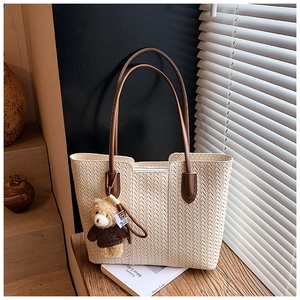 Detailed close-up of woven tote bag with brown leather handles and a cute bear charm detail
