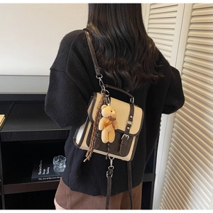 Rear view of a vintage beige and brown crossbody bag with a plush bear charm on a model