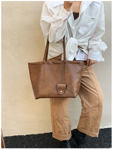 Detail view of a large brown faux leather tote bag with a small decorative charm pendant