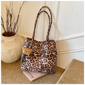 Detail of vintage leopard print tote bag with plush bear charm against a white wall