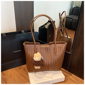 Close-up of brown woven tote bag with two slim straps and a cute plush bear charm