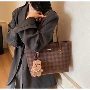 Detail of checkered tote bag with brown leather trim and cute plush bear charm