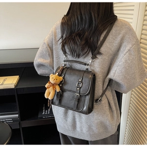 Model wearing a black retro crossbody bag with a cute brown bear pendant in a studio setting