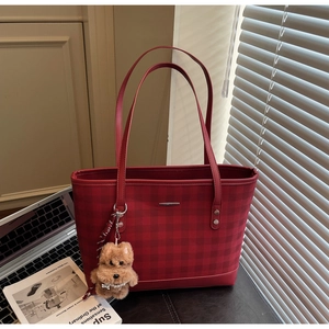 Detail of red plaid tote bag with plush charm and silk scarf on a desk
