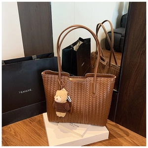 Detail of a brown woven tote bag with a cute teddy bear charm in a lifestyle setting