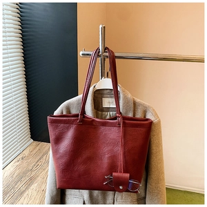 Detail of dark red faux leather tote bag with glasses case charm on beige coat