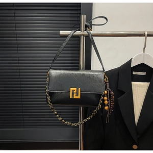 Detail of a black leather shoulder bag with gold geometric buckle and wooden tassel