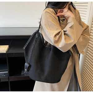 Détail d'un grand cabas noir en daim avec bordure en cuir porté avec un trench-coat kaki
