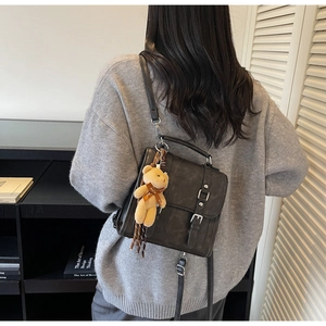 Detail view of a vintage black matte backpack with silver buckles and a cute bear charm