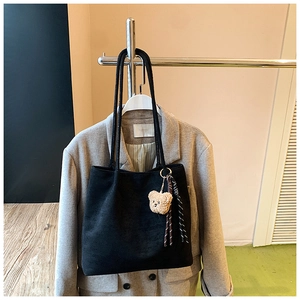 Detail of black tote bag with plush bear charm and striped ribbon on shoulder strap