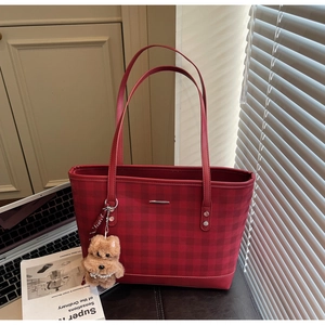 Detail of red checkered tote bag with leather straps and plush puppy charm on a desk