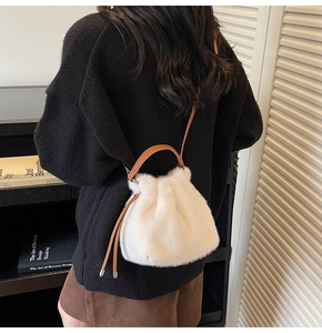 Detail view of a white fuzzy bucket bag with brown leather straps shown on a model