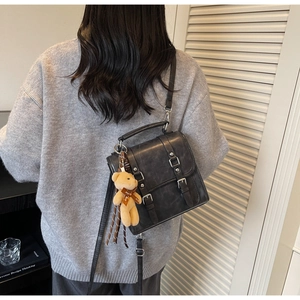 Close-up of vintage black PU leather backpack with silver buckles and plush bear charm
