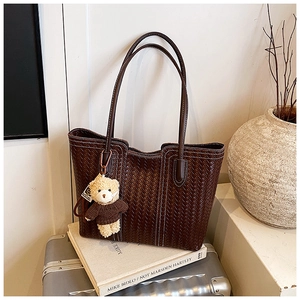 Detail of dark brown woven tote bag with contrast stitching and teddy bear charm