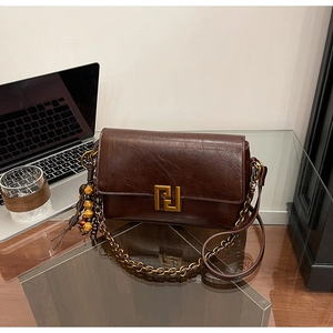 Detail view of brown vintage leather crossbody bag with gold buckle and wooden bead tassel