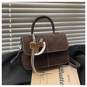 Detail of dark brown matte leather bag with white stitching and horse charm