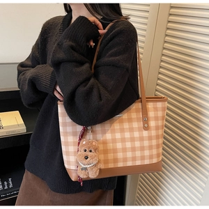 Detailed side view of a brown plaid tote bag with plush dog charm and leather straps