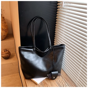 Close-up of black textured leather tote bag with unique glasses holder pendant detail