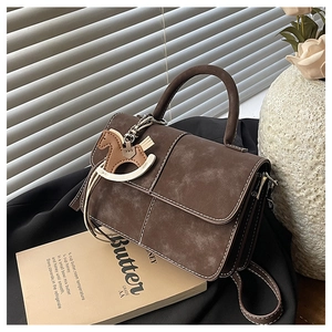 Detail of vintage brown suede handbag with white stitching and horse charm accessory